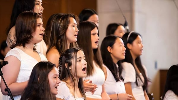 Un grupo de jóvenes estudiantes de la Northfield Mount Hermon School canta juntas en un escenario.