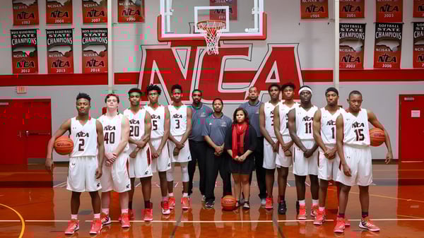 Estudiantes de la Northside Christian Academy posan en la cancha de baloncesto con el branding de la NCAA de fondo.