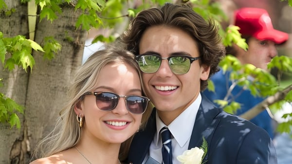 Una pareja sonriente con gafas de sol está frente a un fondo de plantas verdes en el campus de la Northwood School.