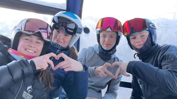Estudiantes de la Northwood School llevan equipo de esquí y forman símbolos de corazón con las manos frente a una ventana cubierta de nieve.