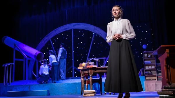 Una mujer está en el escenario de la Norwell District Secondary School frente a un arco azul con decorados en el fondo.