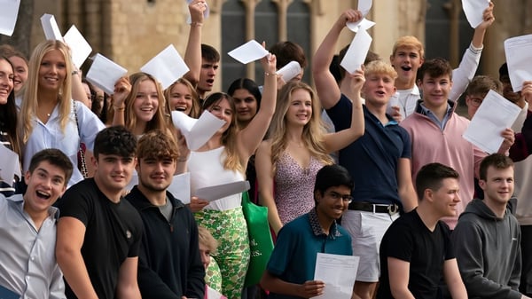 Estudiantes de la Norwich School celebran sus logros académicos frente a un edificio histórico con diplomas en la mano.