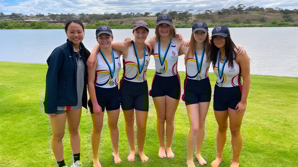 Un grupo de jóvenes atletas está en un campo de césped cerca de un cuerpo de agua en el campus de la Norwood International High School.