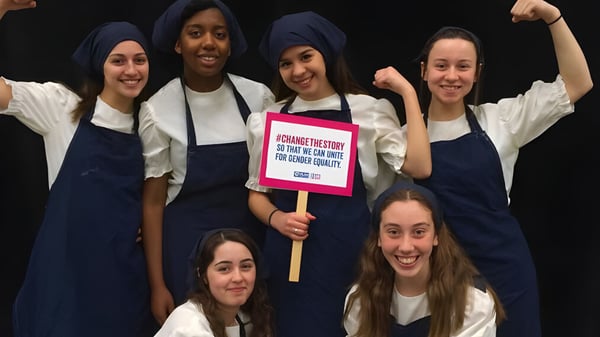 Estudiantes de la Notre Dame High School participan juntos en una demostración en un entorno oscuro con un cartel en las manos.