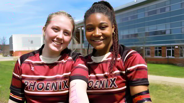 Dos estudiantes de la Nova Scotia School llevan camisetas deportivas a juego y están juntas al aire libre frente a un edificio.