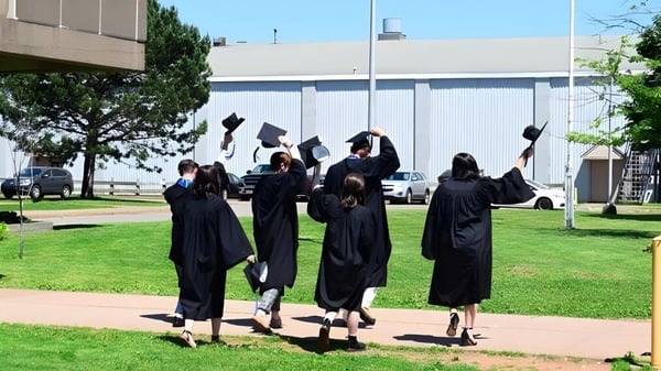 Un grupo de graduadas y graduados del Nova Scotia French Program en togas negras caminan por el campus frente a un gran edificio.