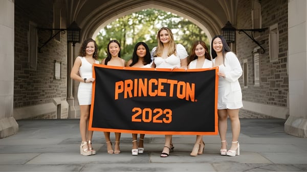 Un grupo de estudiantes de la Oak Mountain Academy se encuentra junto a un gran banner naranja con la inscripción PRINCETON 2023 bajo un arco pintoresco.