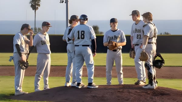 Un grupo de estudiantes de béisbol está de pie en el campo de béisbol del Oak Park Unified School District frente a palmeras y un cielo despejado.
