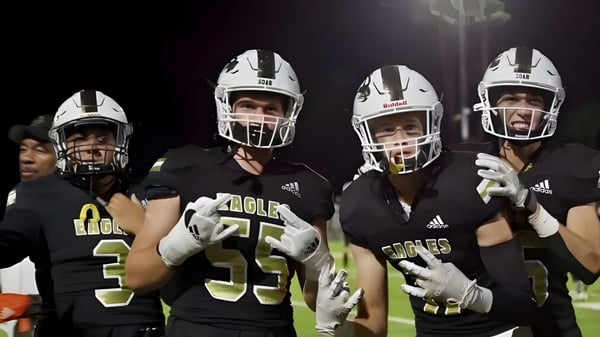 Un grupo de jugadores de fútbol americano en uniforme está de pie en el campo bajo luces brillantes en el terreno del Oak Park Unified School District.