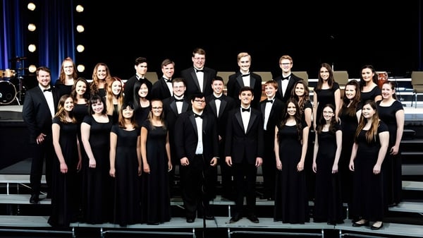 Un gran grupo de estudiantes de Oakland Christian School está vestido formalmente en el escenario bajo los focos.