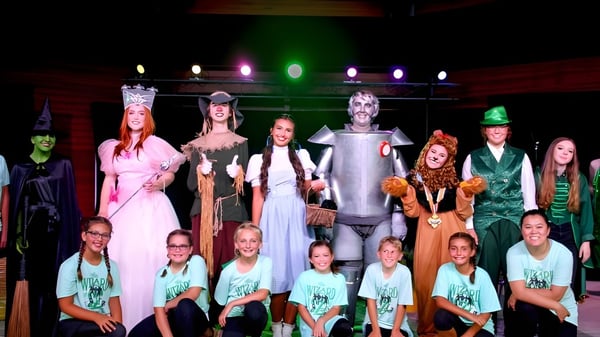 Estudiantes de Oakland Christian School están en disfraces de Halloween en un escenario con iluminación colorida.