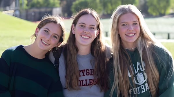 Tres estudiantes con cabello largo y ondulado están juntas en un prado en el terreno de la Oaks Christian School.