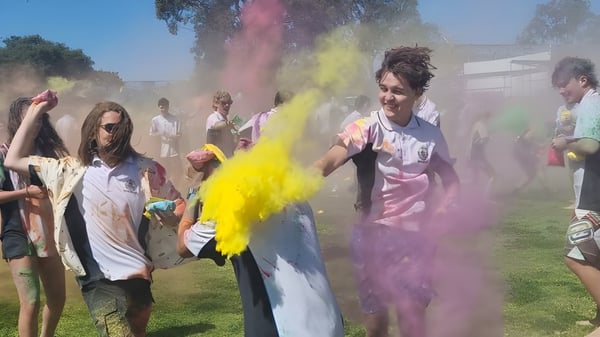 Estudiantes de la Ocean Reef Senior High School lanzan nubes de polvo de colores en un evento al aire libre.