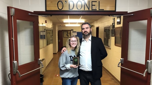 Un hombre y una mujer están en el pasillo de la O'Donel High School frente a un letrero con el nombre de la escuela.