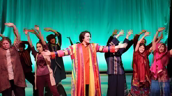 Un grupo de estudiantes de la Okanagan Mission Secondary School actúa en un escenario con fondo verde.