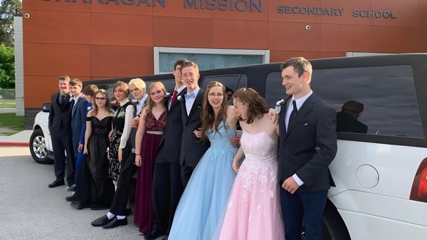 Un grupo de estudiantes está frente al edificio de la Okanagan Mission Secondary School con el nombre de la escuela en la entrada.