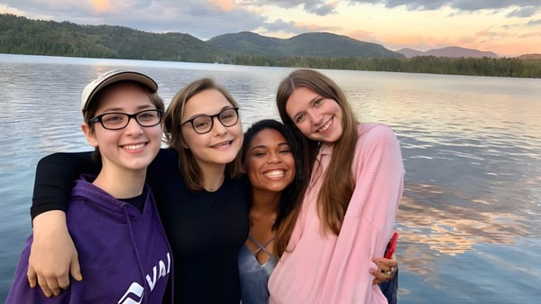 Un grupo de estudiantes de la Oldfields School posa sonriendo frente a un lago con montañas y bosques de fondo.