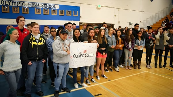 Un grupo de estudiantes del Olympic College se reúne en el gimnasio y sostiene un cartel con el nombre de la escuela.
