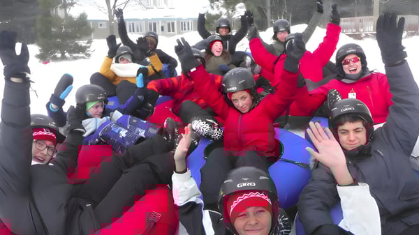 Un grupo de estudiantes de la École secondaire publique Omer-Deslauriers está vestido con colorida ropa de invierno afuera en la nieve frente a edificios.