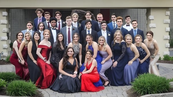 Un grupo de personas vestidas formalmente posan en el exterior de la Ontario Hockey Academy en un camino pavimentado con áreas verdes al fondo.