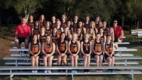 Un grupo de jóvenes deportistas de la Orangewood Christian School están sentadas en gradas al aire libre frente a árboles.