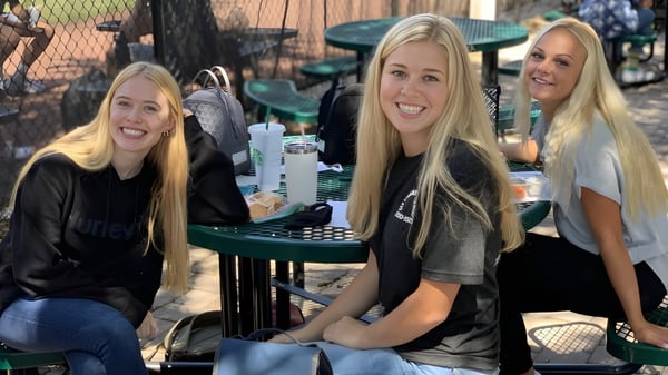 Tres estudiantes con cabello largo y rubio están sentadas en una mesa al aire libre en el campus de la Orangewood Christian School.