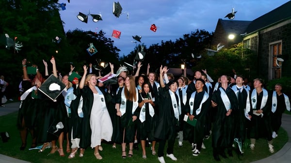 Un grupo de graduadas y graduados de la Oregon Episcopal School está reunido al aire libre por la noche en vestimenta académica.