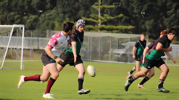 Un grupo de estudiantes juega deportes en el campo deportivo verde del Orewa College con una portería al fondo.