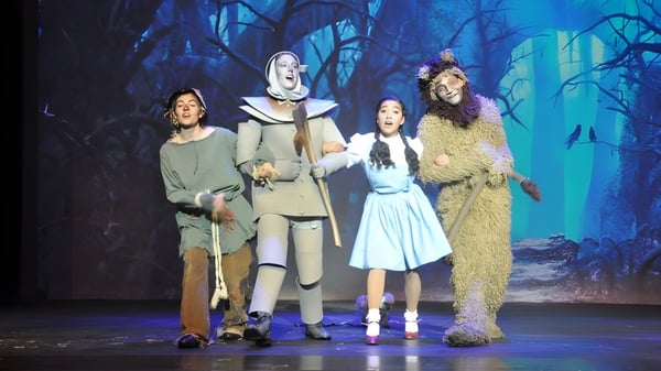 Estudiantes de la Oromocto High School actúan en varios disfraces en un escenario frente a un fondo de bosque oscuro.
