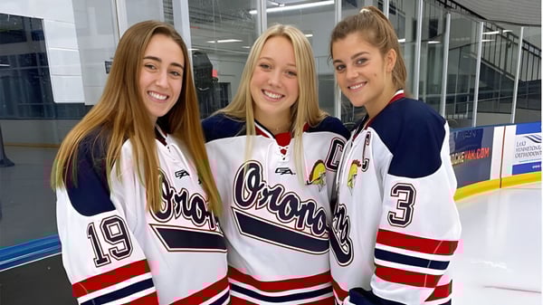 Tres estudiantes de la Orono High School están en camisetas de hockey en la pista de hielo en el gimnasio.