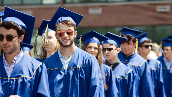 Un grupo de graduadas y graduados de la Osgoode Township High School está frente a un edificio de ladrillo con togas y birretes azules.