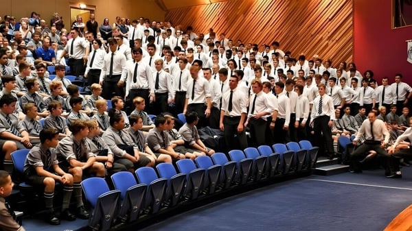 Un grupo de estudiantes está sentado en sillas azules en una sala con paneles de madera en el campus de la Otago Boys' High School.