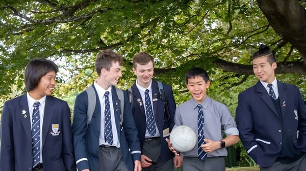 Un grupo de estudiantes de la Otago Boys' High School está juntos en un área exterior verde.