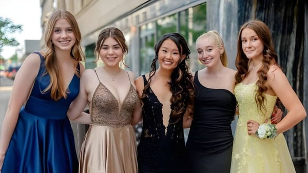 Cinco alumnas de la Otago Girls High School posan sonriendo frente a un edificio con ventanas de vidrio.