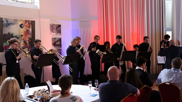 Estudiantes de Oundle School realizan una actuación en un espacio de eventos bien iluminado frente a un público.