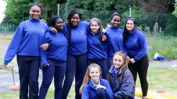 Un grupo de estudiantes de la Our Lady's Bower Secondary School está afuera en un campo con árboles y una cerca de fondo.