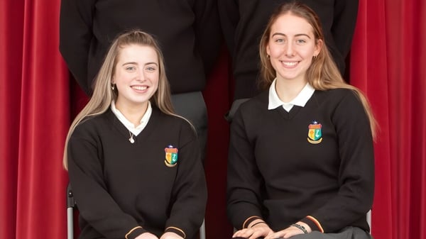 Dos estudiantes en uniformes escolares negros están frente a una cortina roja en el campus de Our Lady’s Secondary School.