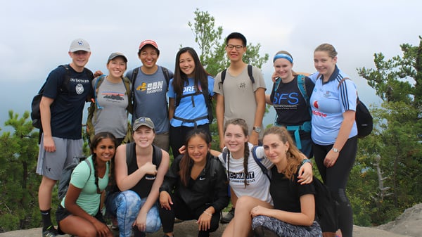 Un grupo de estudiantes de Our Lady’s Secondary School posan juntos al aire libre frente a árboles y un cielo despejado.