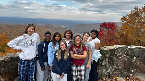 Un grupo de estudiantes de Our Savior New American School está de pie sobre una roca con vista a un colorido paisaje de otoño.