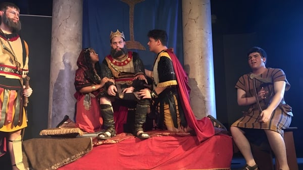 Estudiantes de Our Savior New American School presentan una escena teatral con actores disfrazados en un escenario.