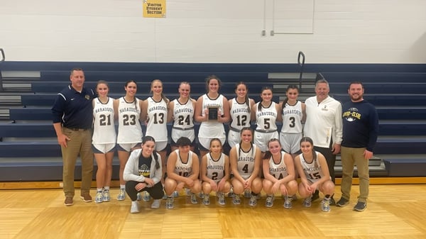 Un grupo de jugadoras de baloncesto y entrenadoras de la Ovid-Elsie High School posan juntas en la cancha de baloncesto.