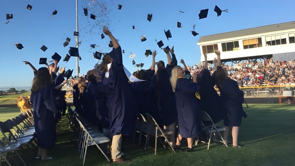 Graduados de la Ovid-Elsie High School lanzan sus gorros al aire y celebran su graduación en el campo deportivo.