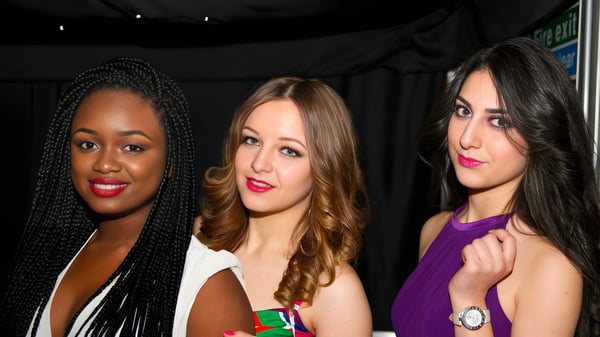 Tres estudiantes con diferentes orígenes posan juntas frente a un fondo oscuro en el Oxford International College.