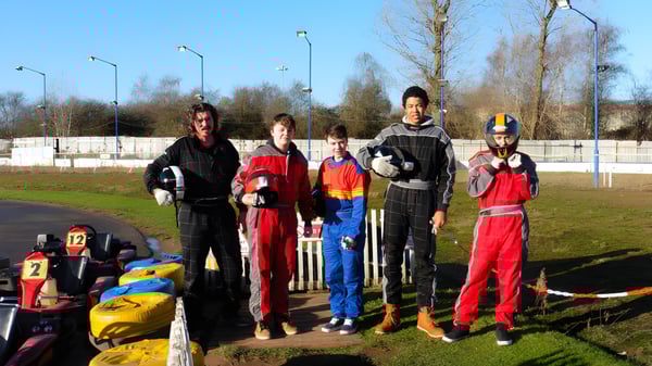 Estudiantes del Oxford Sixth Form College están en trajes de carrera en una pista de carreras frente a un campo de hierba con árboles.