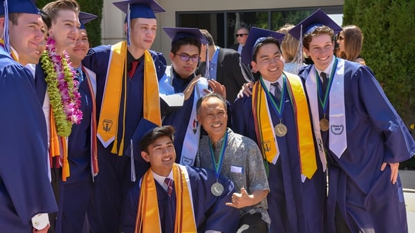 Los graduados de la Pacifica Christian High School están juntos en ropa de graduación morada y dorada durante la ceremonia de graduación.