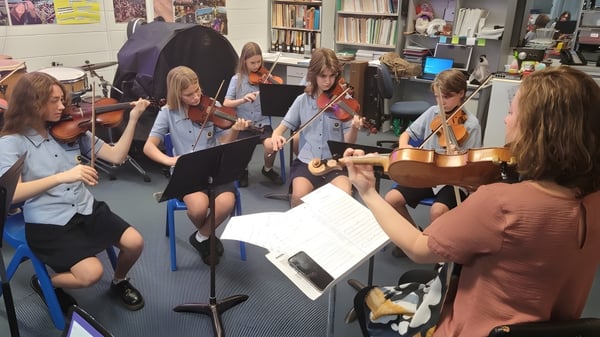 Estudiantes de la Palm Beach Currumbin State High School tocan instrumentos musicales juntos y leen partituras en un aula.