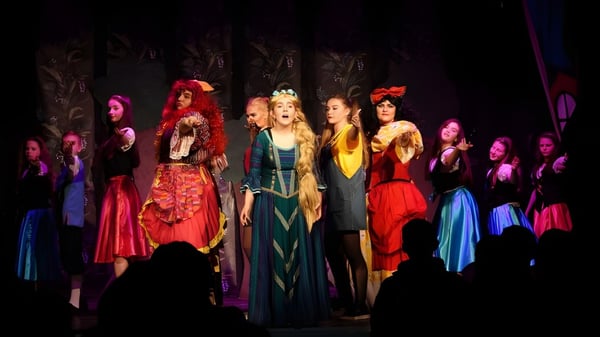 Mujeres en trajes coloridos están en el escenario de la Palmerstown Community School durante una actuación.