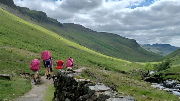 Un grupo de estudiantes del Pangbourne College camina por un sendero rocoso en un paisaje montañoso verde.