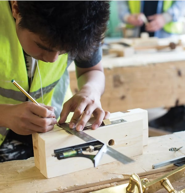 Un aprendiz en la carpintería marca una pieza de trabajo con un ángulo y un lápiz en un taller.