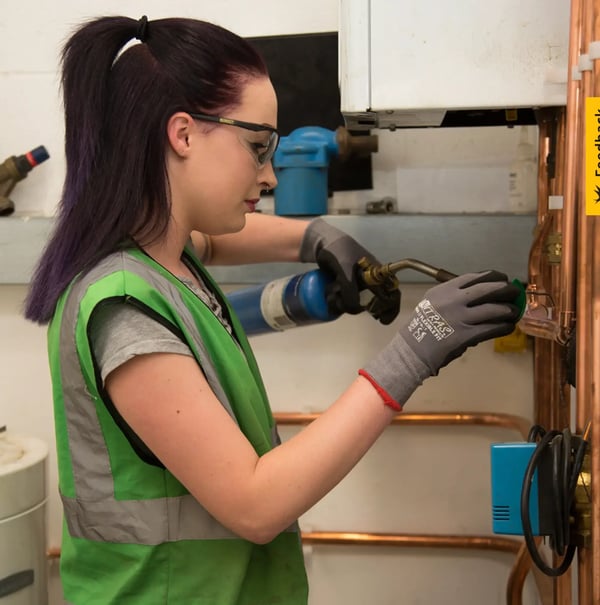 Un aprendiz en el área de tecnología sanitaria y de calefacción trabaja con un quemador en tubos de cobre.